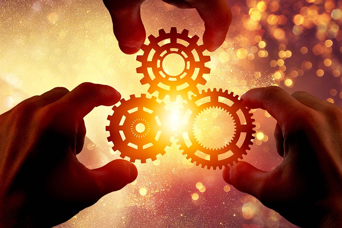 three hands holding gears together