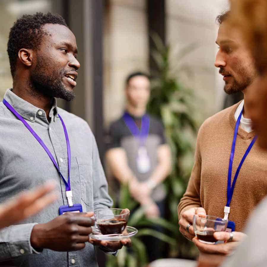 People wearing lanyards and name badges are holding beverages and engaging in conversation at an event