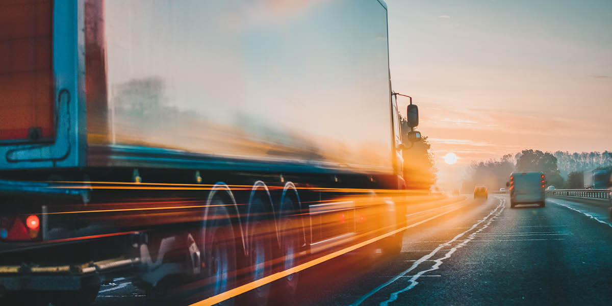 transportation industies represented by a 18-wheeler truck moving fast down a busy highway