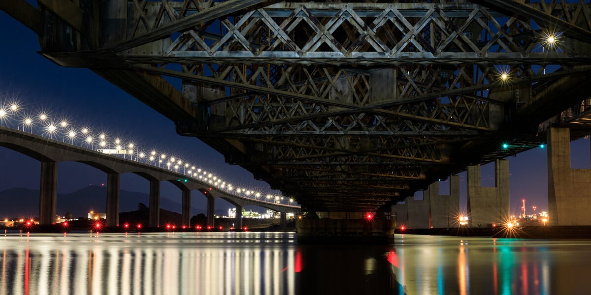 view from below of a bridge over water with a view of a network data center in the background.