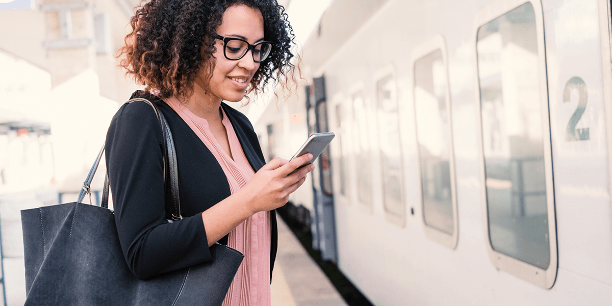 A woman standing on a train platform while looking at her phone and smiling