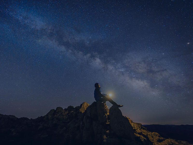 person on mountain looking up at stars