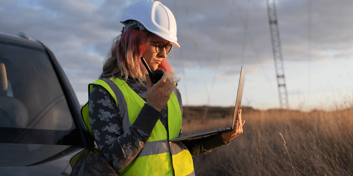 Workers standing in front of a line of windmills while coordinating on a laptop
