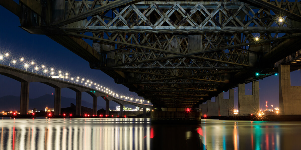 view from below of a bridge over water with a view of a network data center in the background.