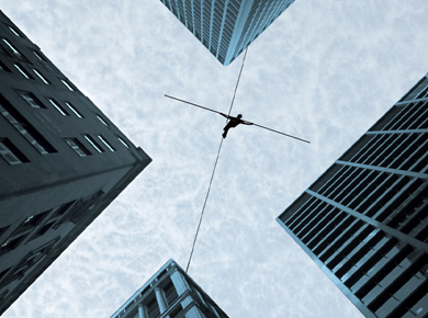 view fromb elow of a man in the city walking on a tight rope holding a blaance bar