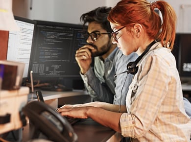 two IT professionals at the computer working together to performing testing for a client
