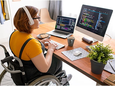 woman in wheelchair seated at desk wearing headphones working in the IT field.