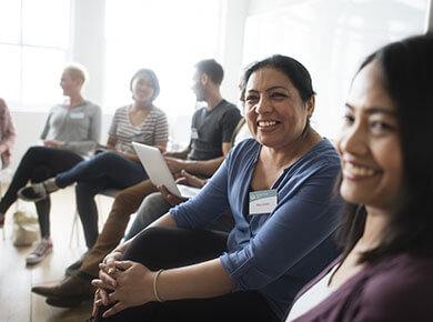 Two women smiling sitting in a row of colleges being recognized