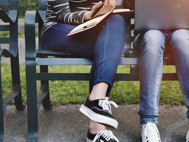 higher education pair sits outside on a bench with laptop