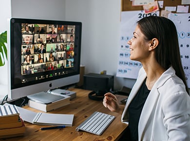 woman seated at desk infront of a mac computer on a video conference call