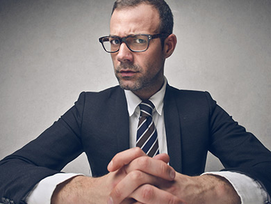 interviewer sits across from table with hands clasped