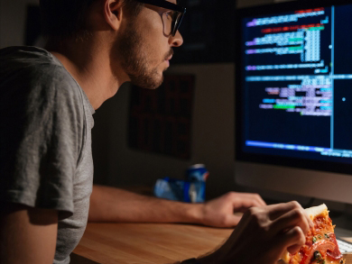 male eats pizza and looks at computer screen code