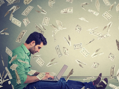 causal male sits on floor with laptop with cash falling around him