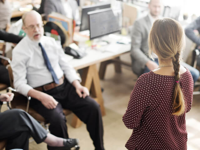 woman standing and facing team of people sitting at their desks