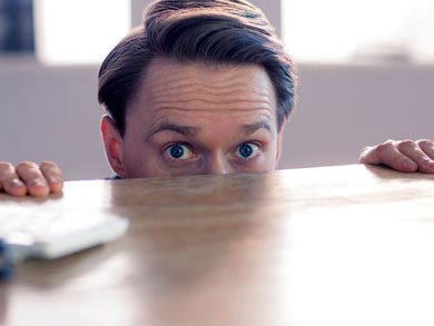 businessman hiding behind a desk peeking up