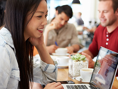 young casual female writing on laptop in coffee shop