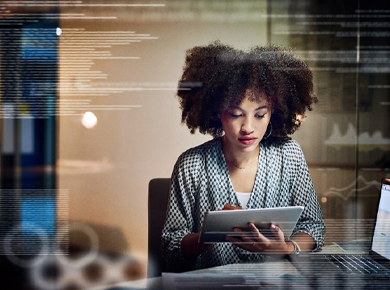 Young female professional seated at workstation in the evening reviewing certifications on a tablet