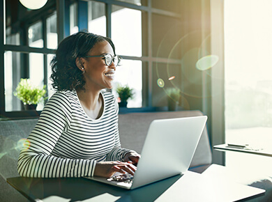 woman wearing glasses and a striped shirt working remotely using a laptop