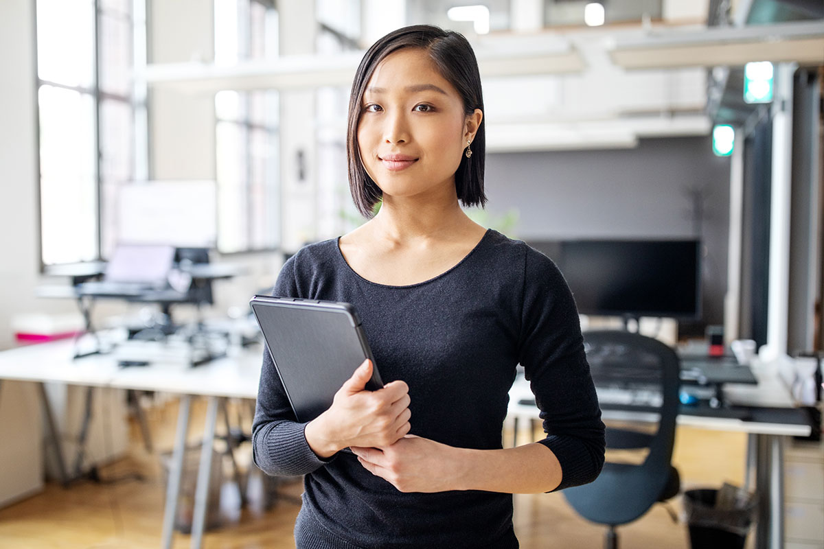 asian-american professional posed in office space holding tablet