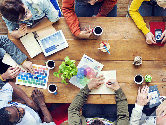 Overhead view of a wooden tabletop with people working in a streamlined design production studio