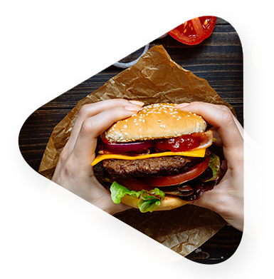 woman holding a deluxe burger over wrapper on table preparing to eat. 