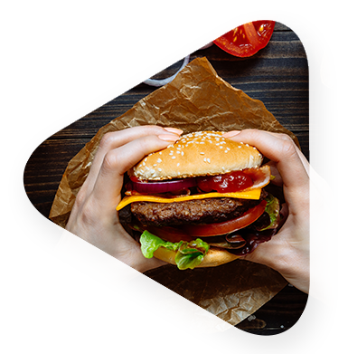 woman holding a deluxe burger over wrapper on table preparing to eat.