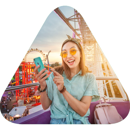 A woman on a theme park ride pointing to her phone with a sunset in the background